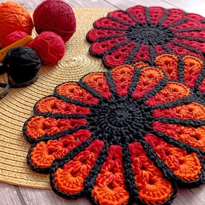 May include: Handmade crochet coasters in a flower design. The coasters feature a black center with orange and red petals. The image also shows balls of yarn in orange and red, a crochet hook, and a measuring tape.