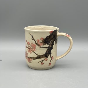 May include: A white ceramic mug with a brown and pink floral design. The mug has a handle and is perfect for enjoying a hot beverage.