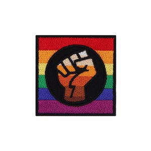 Könnte beinhalten: Ein regenbogenfarbener Patch mit einer schwarzen Faust, die in die Luft erhoben ist. Die Faust ist orange und braun und von einem schwarzen Kreis umgeben.