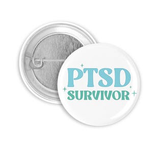 Könnte beinhalten: Weißer Ansteckbutton mit dem Text "PTSD SURVIVOR" in Hellblau und Grün. Der Button hat eine Metallrückseite mit Sicherheitsnadelverschluss. Das Design enthält kleine Kreuzsymbole.
