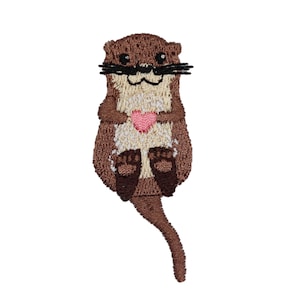 May include: Embroidered patch featuring a brown otter holding a pink heart. The otter has black whiskers and a cream-colored chest. The patch is designed with detailed stitching, perfect for adding to clothing or accessories.