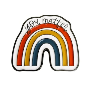 Könnte beinhalten: Ein Emaille-Pin in Regenbogenform mit den Worten "you matter". Der Pin hat rote, gelbe und blaue Bögen, einen weißen Rand und eine schwarze Umrandung. Der Text ist handschriftlich.