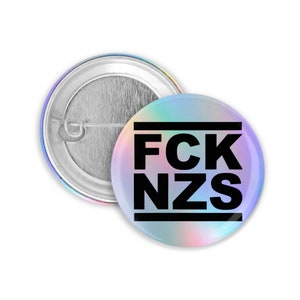 Peut inclure: Un bouton rond avec un fond holographique iridescent et un texte noir qui dit "FCK NZS".