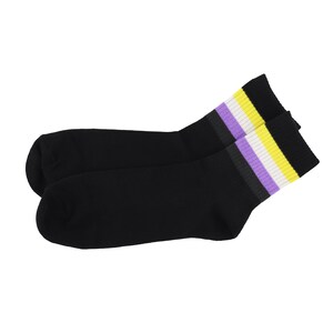Puede incluir: Un par de calcetines negros con un diseño de la bandera del orgullo no binario en el puño. El puño presenta rayas horizontales en los colores de la bandera no binaria: amarillo, blanco, morado y negro. Los calcetines son de material suave.