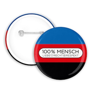 Può includere: Un bottone nero, rosso e blu con il testo "100% MENSCH LIEBE♥RECHT□RESPEKT" in bianco.