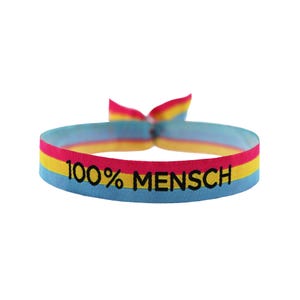 Op de afbeelding: Een kleurrijk geweven armband met een geel, blauw en roze gestreept ontwerp. De armband heeft de tekst "100% MENSCH" in zwart gedrukt.