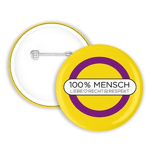 Può includere: Un bottone giallo con un cerchio viola e il testo "100% MENSCH LIEBE ♥ RECHT ✊  RESPEKT"