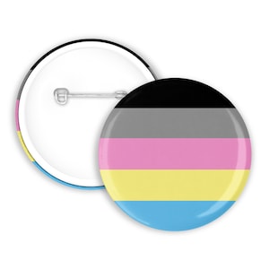 Könnte beinhalten: Ein runder Knopf mit einer Sicherheitsnadel auf der Rückseite, der die Farben der Genderqueer-Pride-Flagge zeigt. Die Flagge hat fünf horizontale Streifen: Schwarz, Grau, Rosa, Gelb und Blau.