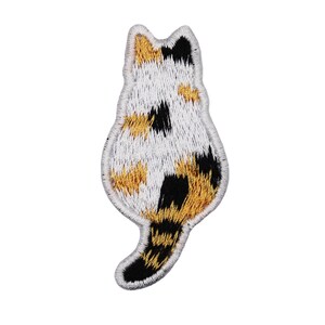Könnte beinhalten: Gestickter Aufnäher mit einem dreifarbigen Kätzchen mit weißem, schwarzem und orangefarbenem Fell. Die Katze ist mit dem Schwanz um den Körper gewickelt vom Betrachter abgewandt.
