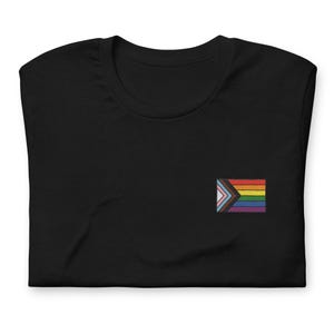 Puede incluir: Camiseta negra con una pequeña bandera del orgullo bordada con una variedad de colores, incluyendo rosa, azul, blanco, negro, marrón, amarillo, naranja y verde.