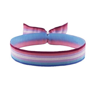 Könnte beinhalten: Ein mehrfarbiges gewebtes Armband mit rosa, blauen, weißen und violetten Streifen. Das Armband ist zu einem Knoten gebunden.