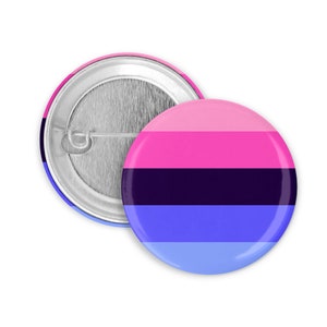 Peut inclure: Deux badges ronds aux couleurs du drapeau de la fierté Omnisexuelle. Les badges présentent un motif de rayures horizontales roses, magenta, noires et bleues. Le dos d'un badge est visible, montrant l'épingle et le support métallique.