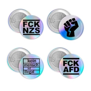 Könnte beinhalten: Satz von vier runden Ansteckbuttons mit holografischen, irisierenden Hintergründen. Die Buttons zeigen schwarzen Text mit der Aufschrift "FCK NZS", eine schwarze Faust mit Blitz, "kein mensch ist illegal" und "FCK AFD".
