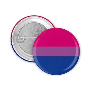 Könnte beinhalten: Ein runder Knopf mit einem bisexuellen Pride-Flaggen-Design. Der Knopf ist rosa, lila und blau. Der Knopf ist an einer silbernen Sicherheitsnadel befestigt.