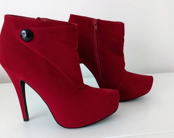 May include: A pair of red suede ankle boots with a high heel and a platform sole. The boots have a zipper on the side and a button detail on the back.