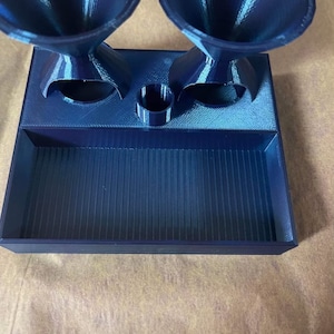 Op de afbeelding: Een blauwe 3D-geprinte lade met twee trechters en een kleine cilinder. De lade heeft een getextureerd oppervlak en de trechters hebben een gestreept patroon.