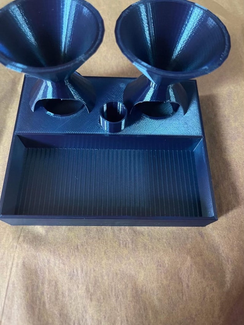 Op de afbeelding: Een blauwe 3D-geprinte lade met twee trechters en een kleine cilinder. De lade heeft een getextureerd oppervlak en de trechters hebben een gestreept patroon.