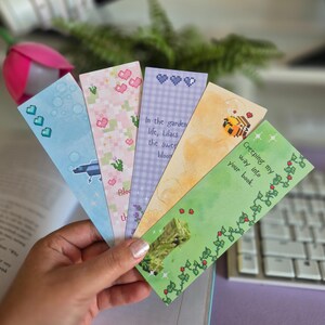 May include: Set of five colourful bookmarks with pixelated designs and inspirational quotes. The bookmarks feature a bee, a flower, a garden, and a vine. The quotes include "In the garden life, Lilacs the sweet bloom", "Creeping my way into your book", and "Blooming the"