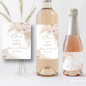 Puede incluir: Etiquetas de botellas de vino de boda con un dise&ntilde;o boho chic con hierba de pampa seca y flores rosa claro. Las etiquetas dicen "Cheers to love and happiness" con los nombres "Aloke y Mukul" y la fecha "May 25, 2025".