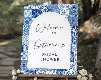 Op de afbeelding: Welkom bij Olivia's Bridal Shower bord met een blauwe en witte gepatroneerde achtergrond. Het bord staat op een houten ezel.