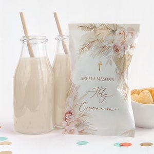 May include: A white favor bag with a watercolor design of pampas grass, roses, and a gold cross. The bag says "Angela Mason's Holy Communion" in gold lettering.