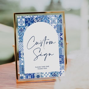May include: A gold-framed sign with a blue and white patterned border. The sign says "Custom Sign" and "Please take one, thank you!"