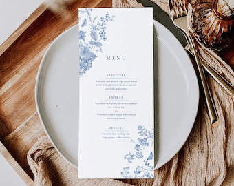 May include: A white menu card with blue floral designs and text. The menu includes appetizers, entrees, and desserts. The text reads: "MENU", "APPETIZER", "Artichoke and spinach dip, tuscan bread served with a delicious blend of spinach, artichoke and cream", "ENTRÉE", "Succulent beef prime rib served medium rare with as jus", "Frenched chicken breast with roasted rosemary potatoes", "DESSERT", "Coconut layer wedding cake", "Lime gelato, coffee and tea".