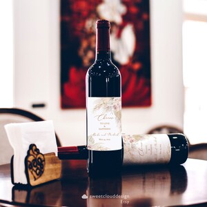Puede incluir: Dos botellas de vino con etiquetas personalizadas que presentan un dise&ntilde;o floral y el texto "Cheers to love and happiness". Las etiquetas tambi&eacute;n incluyen los nombres "Aloke y Mukut" y la fecha "May 23, 2021".