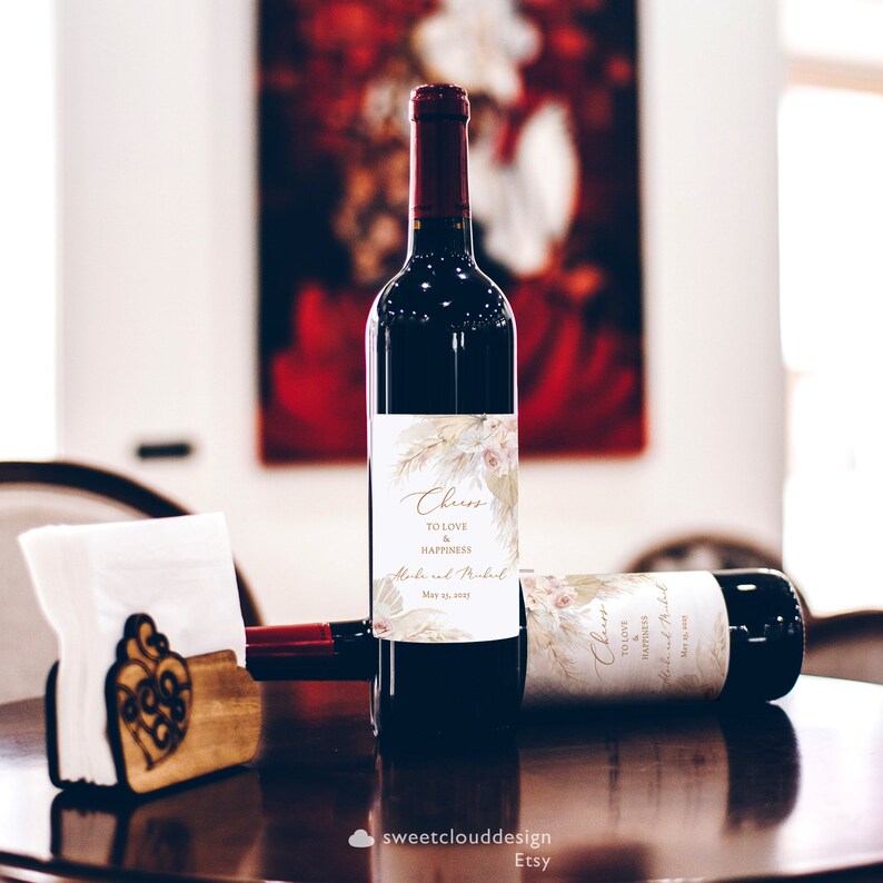 Puede incluir: Dos botellas de vino con etiquetas personalizadas que presentan un dise&ntilde;o floral y el texto "Cheers to love and happiness". Las etiquetas tambi&eacute;n incluyen los nombres "Aloke y Mukut" y la fecha "May 23, 2021".
