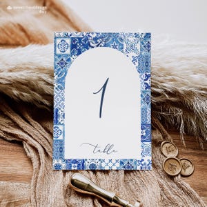 May include: Blue and white tile patterned table number card with the number "1" and the word "table" written in cursive.