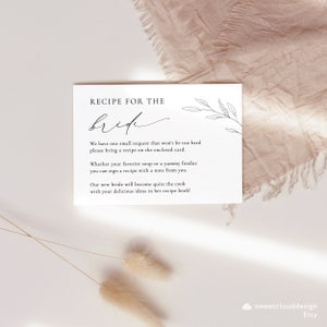 May include: A white card with black text that reads "Recipe for the Bride". The card has a simple floral design and instructions for guests to bring a recipe for the bride.