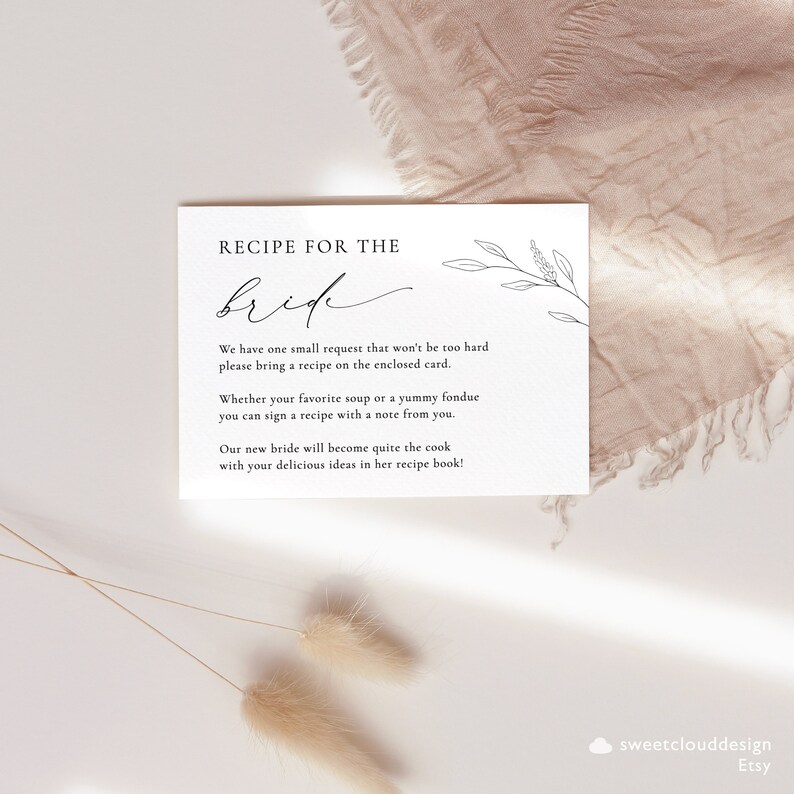 May include: A white card with black text that reads "Recipe for the Bride". The card has a simple floral design and instructions for guests to bring a recipe for the bride.