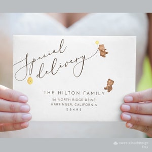 May include: A white envelope with the text "Special Delivery" in cursive script. The envelope has two small brown bear illustrations with yellow balloons and a small illustration of a honeycomb. The text "THE HILTON FAMILY" is printed in black below the illustrations, followed by the address "56 NORTH RIDGE DRIVE, HARTINGER, CALIFORNIA 28495".