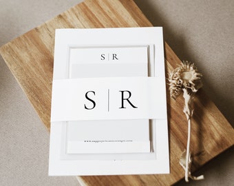 以下が含まれることがあります： シンプルなデザインの白い結婚式の招待状で、黒い文字で「S|R」のイニシャルが書かれています。招待状は木製の表面に置かれています。