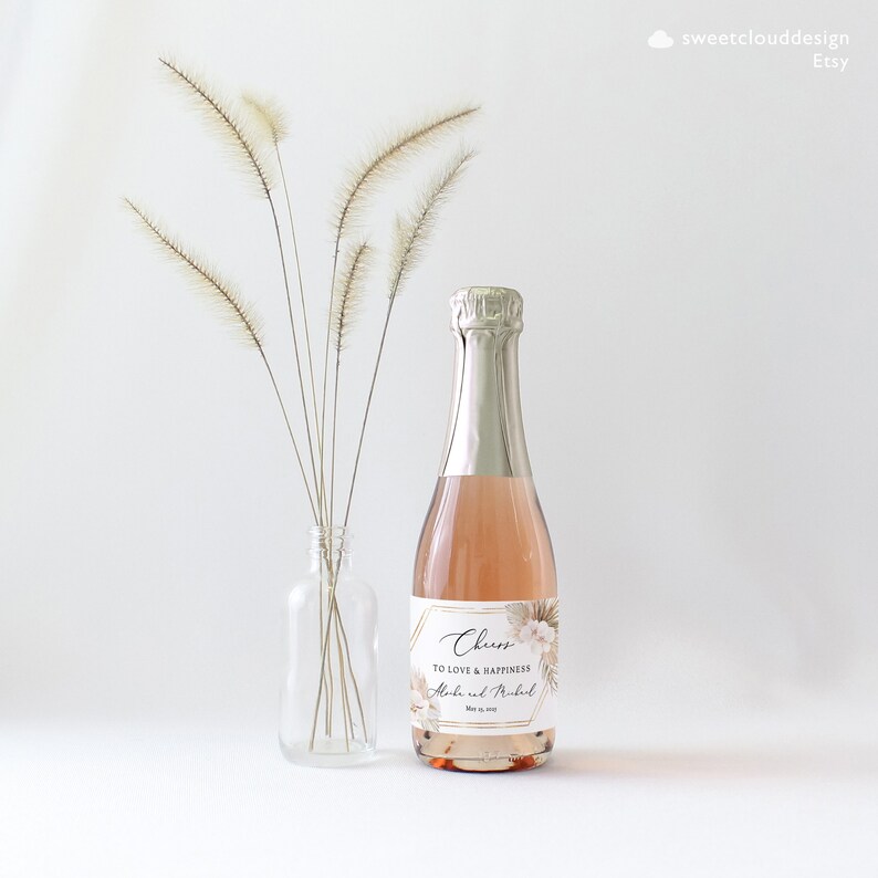 May include: A small bottle of champagne with a gold and white label that says "Cheers to love and happiness" with the names "Alisha and Michael" and the date "May 12, 2019".