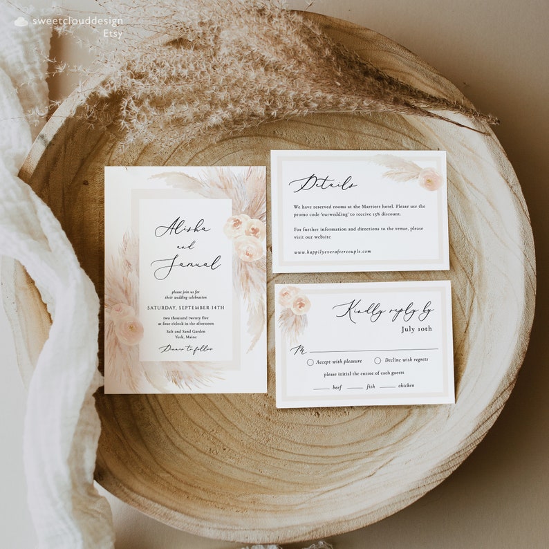 May include: Wedding invitation suite with a boho theme. The invitation features a watercolor illustration of pampas grass and flowers in shades of beige and white. The text reads "Alisha and Jamal" and includes the date and time of the wedding. The RSVP card includes a choice of "Accept with pleasure" or "Decline with regrets" and a meal selection of beef, fish, or chicken.