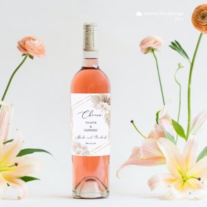 May include: A rose gold and white wedding wine bottle label with a floral design and the text "Cheers to love and happiness" and "[Name] and [Name] May 15, 2021".
