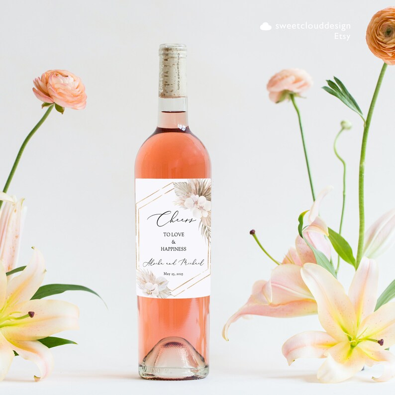 May include: A rose gold and white wedding wine bottle label with a floral design and the text "Cheers to love and happiness" and "[Name] and [Name] May 15, 2021".