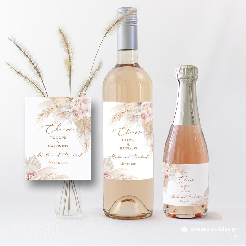 Puede incluir: Etiquetas de botellas de vino de boda con un dise&ntilde;o boho chic con hierba de pampa seca y flores rosa claro. Las etiquetas dicen "Cheers to love and happiness" con los nombres "Aloke y Mukul" y la fecha "May 25, 2025".