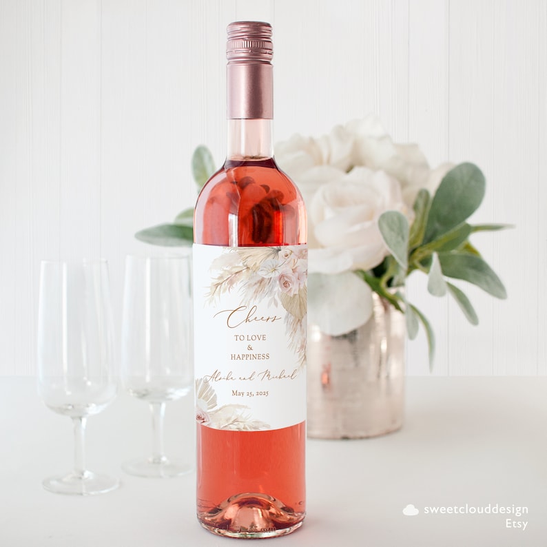 Puede incluir: Una botella de vino rosado con una etiqueta blanca que presenta un dise&ntilde;o floral y el texto "Cheers to love & happiness" con los nombres "Alexa y Michael" y la fecha "May 21, 2023".