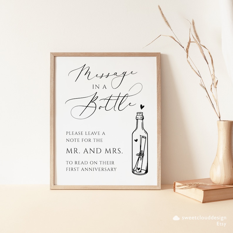 May include: A black and white sign with the text "Message in a Bottle" and a drawing of a bottle with a rolled up note inside. The sign says "Please leave a note for the Mr. and Mrs. to read on their first anniversary."