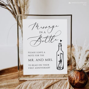 May include: A white sign with black text that reads "Message in a Bottle" with a drawing of a bottle with a rolled up note inside. The sign also says "Please leave a note for the Mr. and Mrs. to read on their first anniversary."