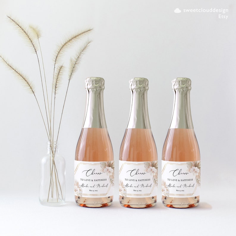 May include: Three mini champagne bottles with gold foil labels. The labels have a geometric design with a floral pattern and the text "Cheers to love and happiness" with a name and date.