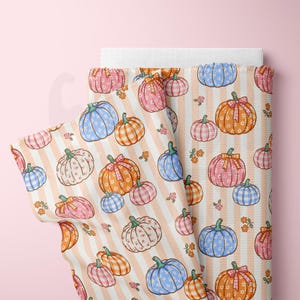 May include: A roll of fabric featuring a repeating pattern of pumpkins in various colors, including blue, pink, and orange, with floral details. The pumpkins are set against a backdrop of vertical peach stripes.