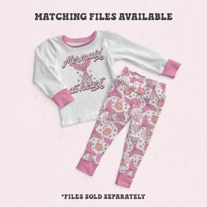 May include: White long-sleeved shirt with pink trim and a pink mermaid graphic that says "Mermaid at heart". Matching pink pants with a mermaid tail and seashell pattern.