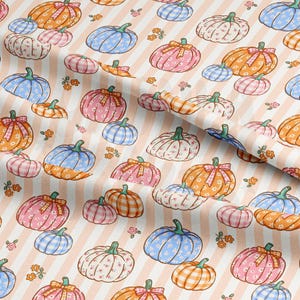 May include: Fabric with a repeating pattern of pumpkins in various sizes and colors, including orange, pink, blue, and white. The pumpkins have different patterns and are set against a peach and white striped background. Small floral accents are scattered throughout.