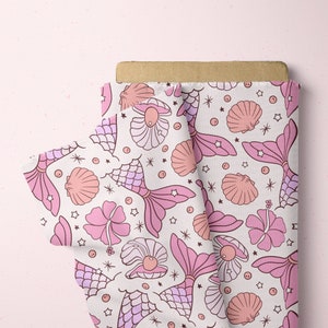 May include: Pink fabric with a repeating pattern of mermaids, seashells, and stars. The mermaids are pink and have a tail with scales. The seashells are pink and white. The stars are white.