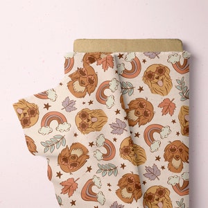 May include: A beige fabric with a repeating pattern of brown dogs wearing sunglasses, rainbows, and stars. The fabric is folded in half, showing the pattern on both sides.