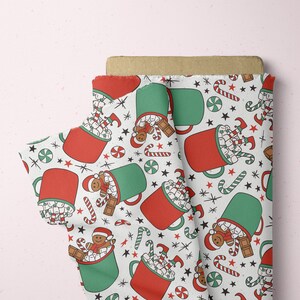 May include: White fabric with a repeating pattern of red and green mugs filled with marshmallows and candy canes. The mugs have a gingerbread man and a candy cane on the side. There are also red stars and green peppermint candies in the pattern.