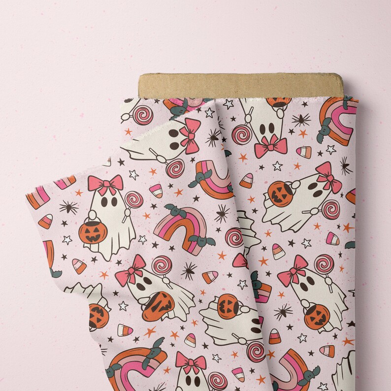 Pode incluir: Um rolo de tecido com um padr&atilde;o repetitivo com tema de Halloween. O design apresenta fantasmas de desenhos animados com la&ccedil;os rosa, segurando ab&oacute;boras e pirulitos, juntamente com arco-&iacute;ris, estrelas, doces de milho e morcegos em um fundo rosa claro.